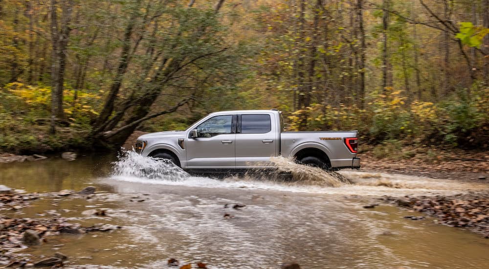 A silver 2021 Ford F-150 Tremor is shown from the side while driving through mud.