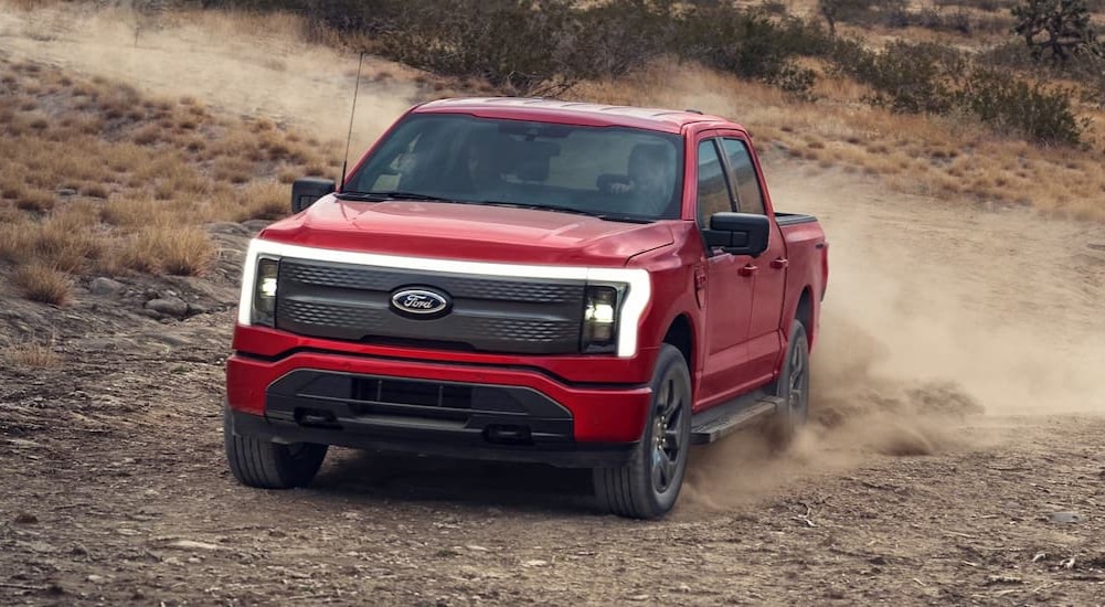 A red 2023 Ford F-150 Lightning is shown driving on sand.
