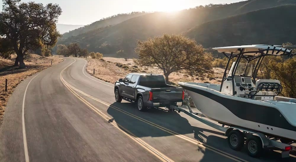 A gray 2023 Toyota Tundra Hybrid is shown towing a boat on a highway.