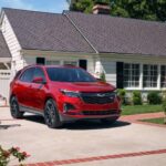 A red 2024 Chevy Equinox RS is shown parked on a driveway near a family.