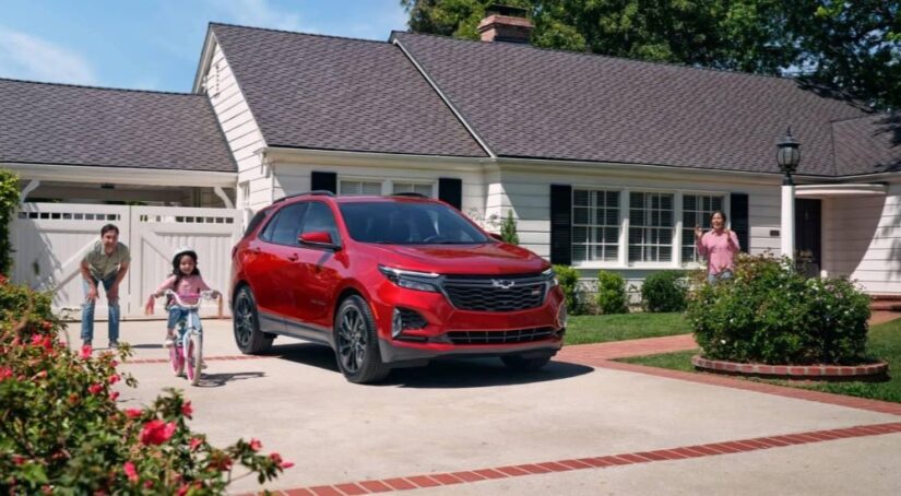 A red 2024 Chevy Equinox RS is shown parked on a driveway near a family.
