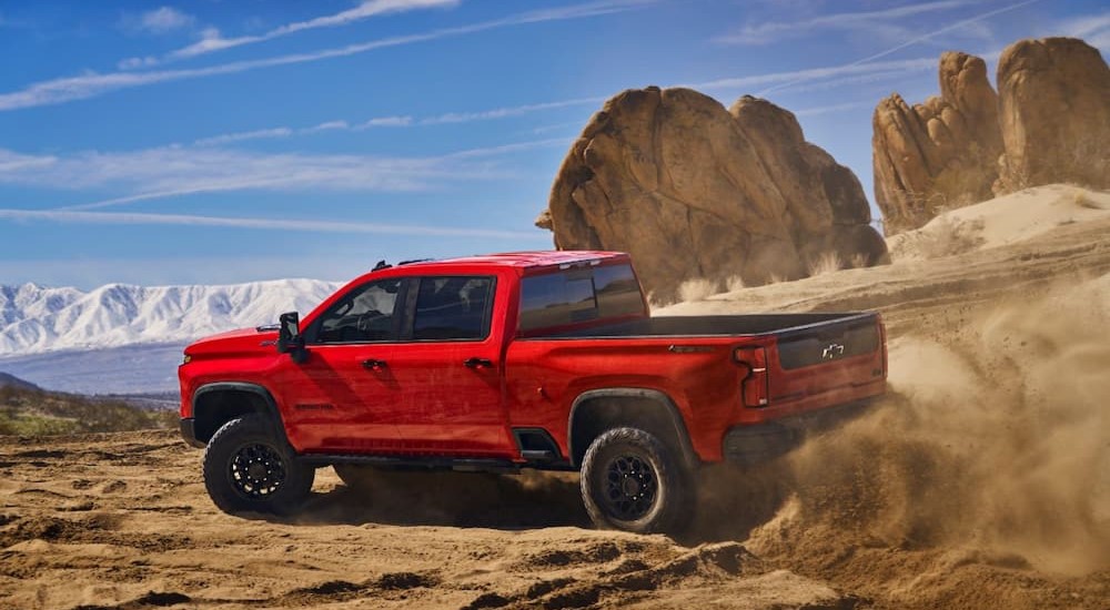A red 2024 Chevy Silverado 2500 HD ZR2 is shown driving off-road on sand.