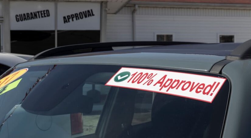 A 100% approved sticker is shown on a windshield at a Buy Here Pay Here dealership.