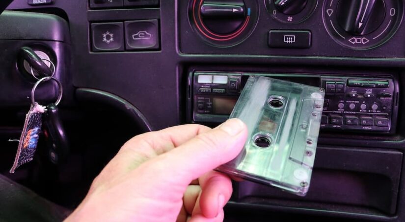 A person is shown putting a cassette tape into a car radio.