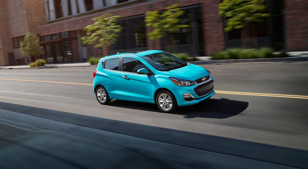 A teal 2021 Chevy Spark is shown driving on a city street.