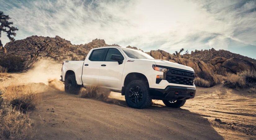 A white 2023 Chevy Silverado 1500 Z71 Trail Boss is shown kicking up dust after leaving a Chevy Silverado 1500 dealer.