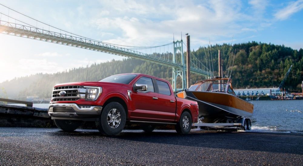 A red 2023 Ford F-150 is shown towing a boat near a bridge.