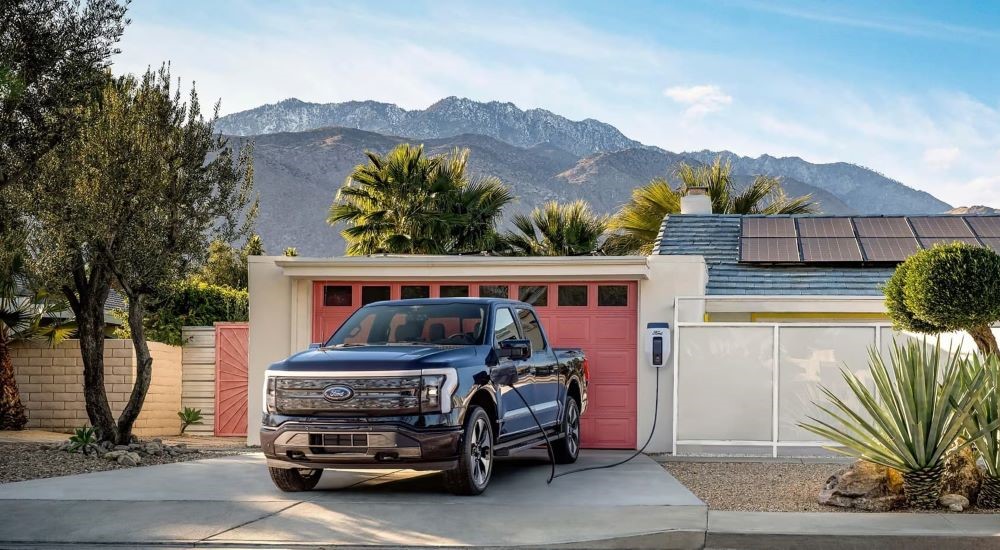 A black 2022 Ford F-150 Lightning is shown charging in a driveway.