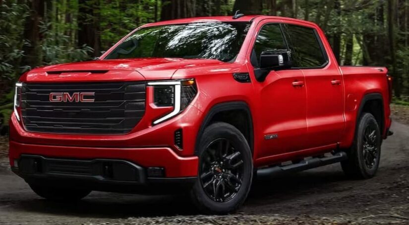 A popular GMC for sale, a red 2023 GMC Sierra 1500, is shown parked off-road in a forest.
