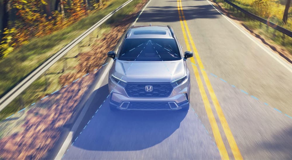 A silver 2023 Honda CR-V Hybrid Sport Touring is shown with simulated sensor lines on a highway.