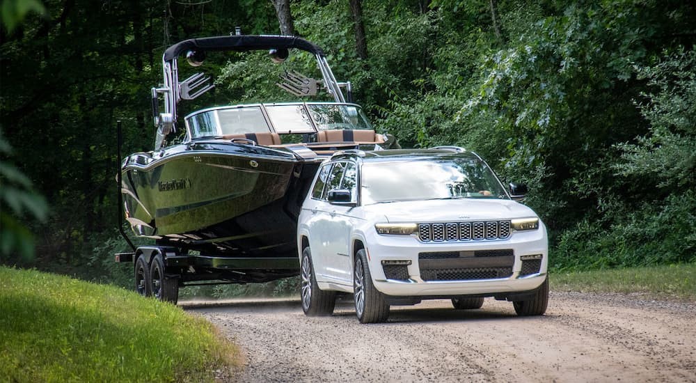 A white 2023 Jeep Grand Cherokee is shown towing a boat off-road.