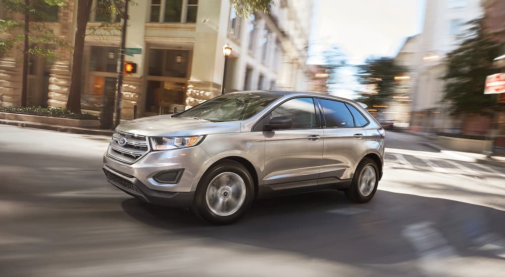 A silver 2018 Ford Edge is shown driving on a city street.
