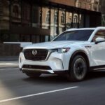 A white 2024 Mazda CX-90 for sale near Lexington, SC is shown driving on a city street