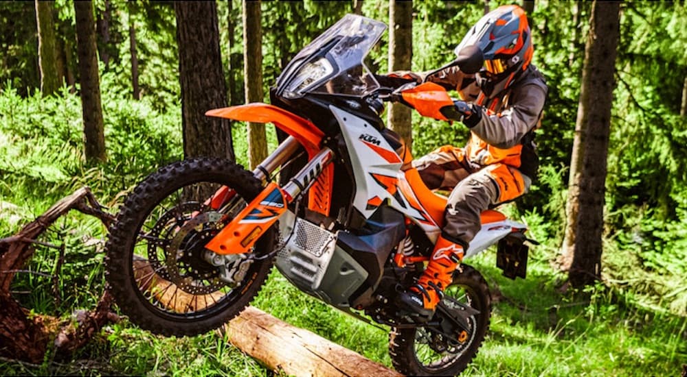 An orange 2023 KTM 890 Adventure R is shown jumping in the forest.