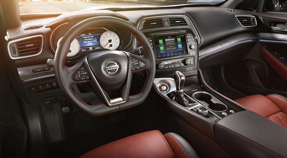 The black and red interior of a 2021 Nissan Maxima is shown from the driver's seat.