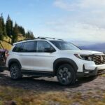 A white 2023 Honda Passport Elite is shown towing an ATV on a trail.