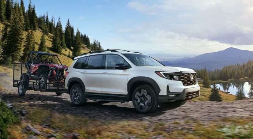 A white 2023 Honda Passport Elite is shown towing an ATV on a trail.