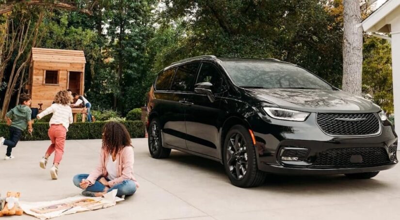 A black 2023 Chrysler Pacifica is shown parked on a driveway near children playing.
