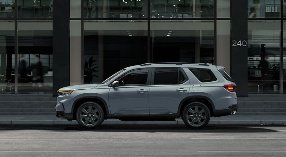 A grey 2023 Honda Pilot Sport is shown parked in front of a city building.