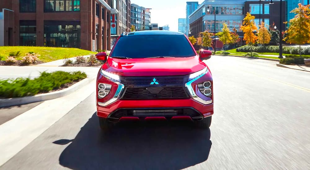 A red 2023 Mitsubishi Eclipse Cross is shown driving on a city street.