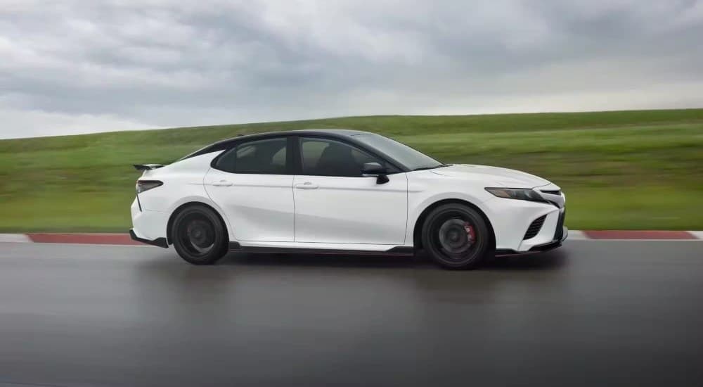 A white 2023 Toyota Camry TRD is shown driving on a racetrack.