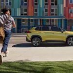 A yellow 2023 Toyota Corolla Cross Hybrid is shown parked near a colorful building.