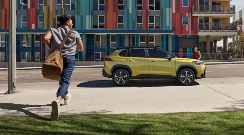 A yellow 2023 Toyota Corolla Cross Hybrid is shown parked near a colorful building.