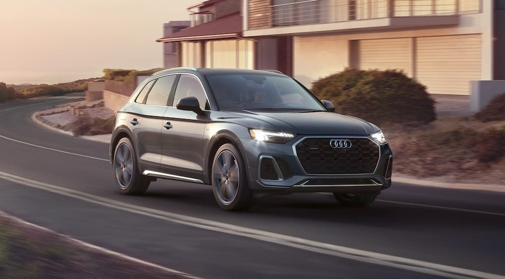 A gray 2023 Audi Q5 is shown driving on a road near a house.