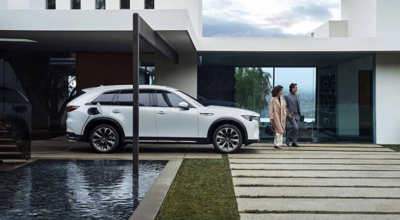 A white 2024 Mazda CX-90 PHEV, is shown charging at a couples home.