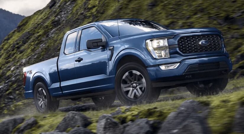 A blue 2023 Ford F-150 STX is shown from the side while off-road after winning a 2023 Ford F-150 vs 2023 Nissan Titan comparison.