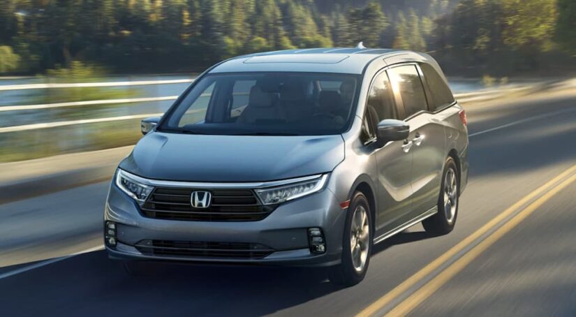 A popular Honda Odyssey for sale, a gray 2023 Honda Odyssey Elite, is shown driving on a highway.