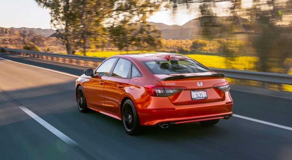 A red 2023 Honda Civic SI is shown from a rear angle driving on a road.