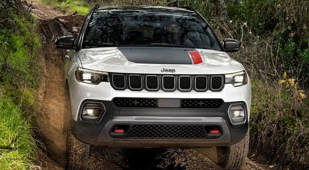 A white 2023 Jeep Compass Trailhawk is shown driving on a muddy path.
