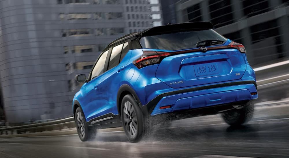 A blue 2023 Nissan Kicks is shown driving on a wet road from a rear angle.