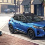 A blue 2023 Nissan Kicks for sale is shown parked near a café.