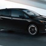 A black 2024 Nissan LEAF is shown driving on a road to visit a Nissan LEAF for sale.
