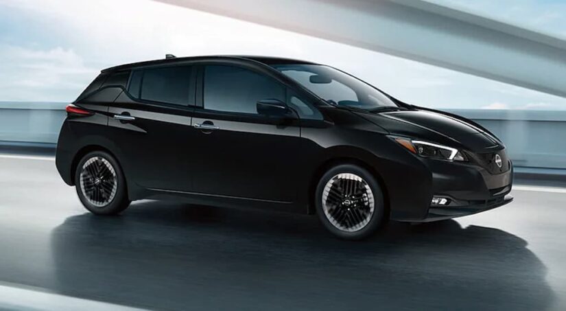 A black 2024 Nissan LEAF is shown driving on a road to visit a Nissan LEAF for sale.