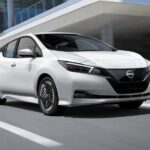 A white 2023 Nissan LEAF for sale is shown driving on a city street.