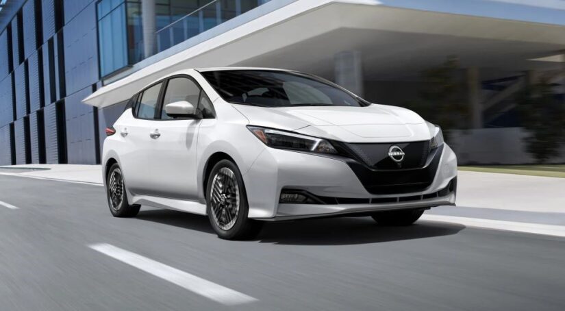 A white 2023 Nissan LEAF for sale is shown driving on a city street.