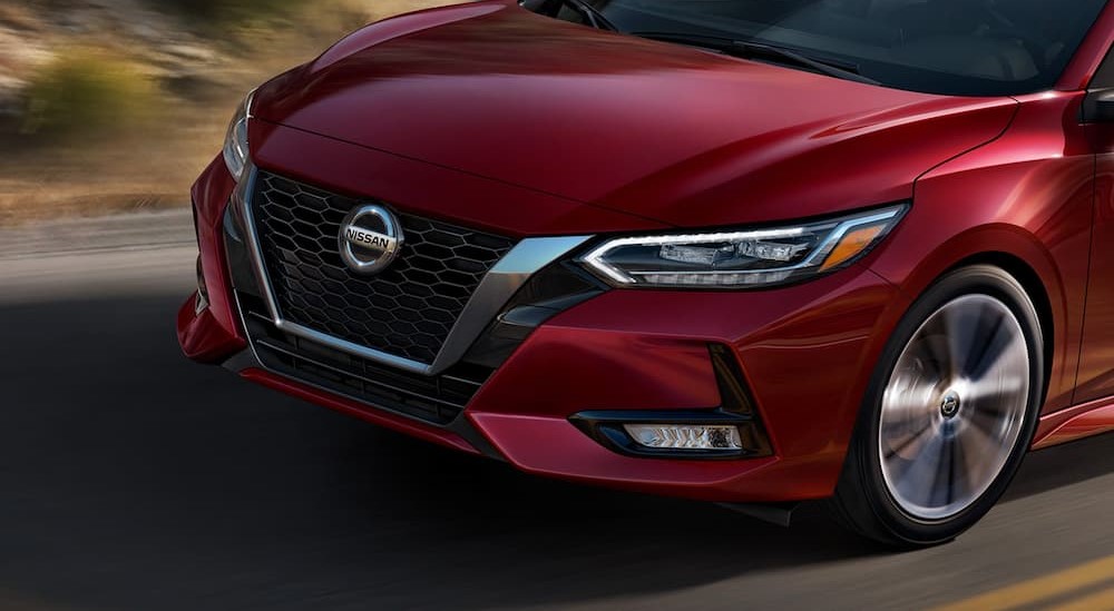 A red 2023 Nissan Sentra is shown driving on a highway from a front angle.