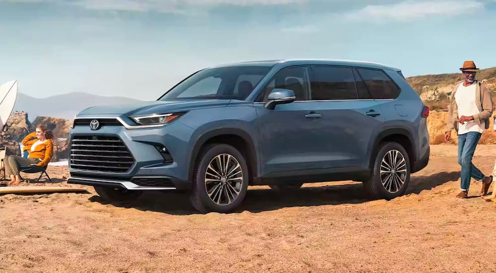 A blue 2024 Toyota Grand Highlander is shown parked on sand.