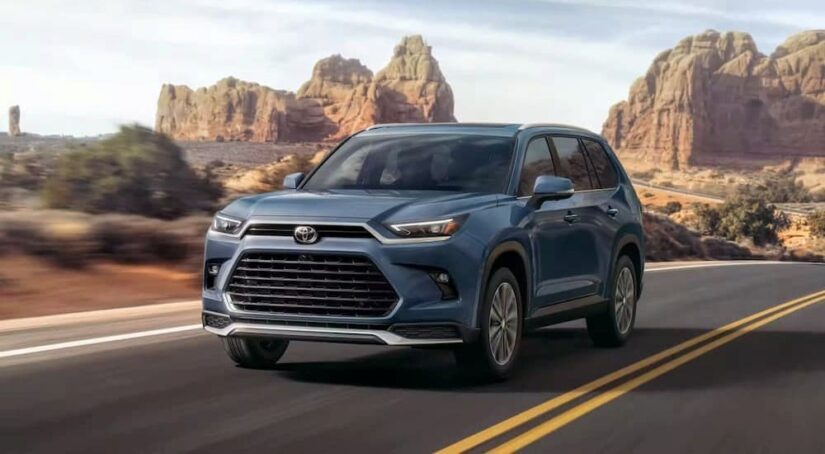 A blue 2024 Toyota Grand Highlander is shown driving on a highway after visiting a Toyota dealer.