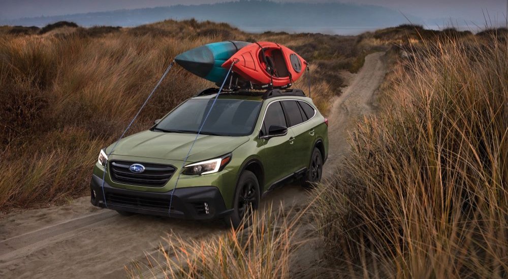 A green 2022 Subaru Outback is shown on a path with kayaks on the roof.