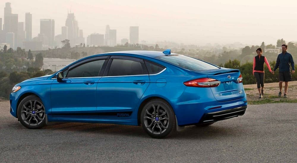 A blue 2020 Ford Fusion is shown parked near a city.