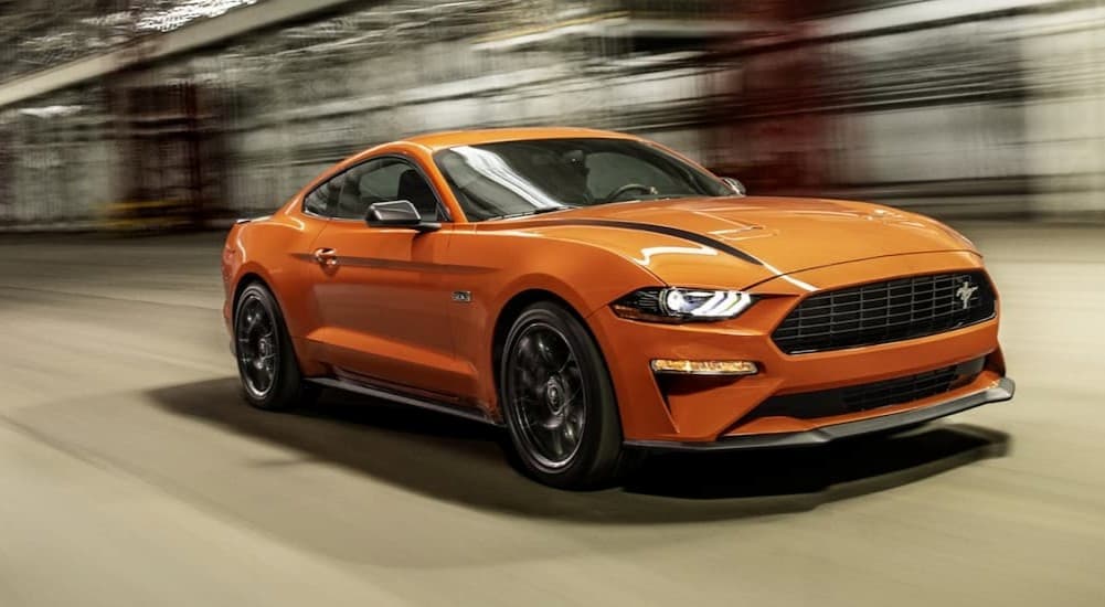 An orange 2021 Ford Mustang is shown driving on a city street.