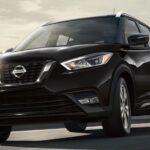 A black 2023 Nissan Kicks SV is shown driving away from a cityscape on a bridge.