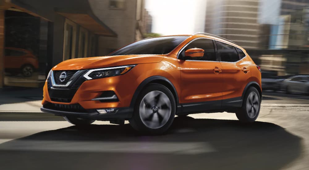 An orange 2020 Nissan Rogue Sport is shown driving through a city intersection.