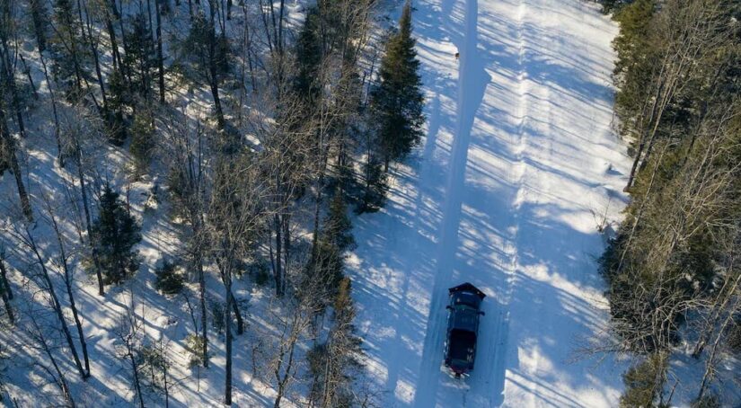Fresh from a used commercial vehicle dealer, a black 2023 Chevy Silverado 1500 HD, is shown from high above plowing a snowy road.