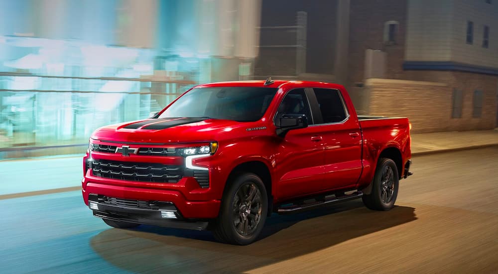 A red 2023 Chevy Silverado 1500 RST is shown driving on a city street.