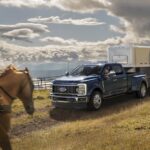 A blue 2023 Ford F-250 Super Duty is shown parked off-road while towing a horse trailer.